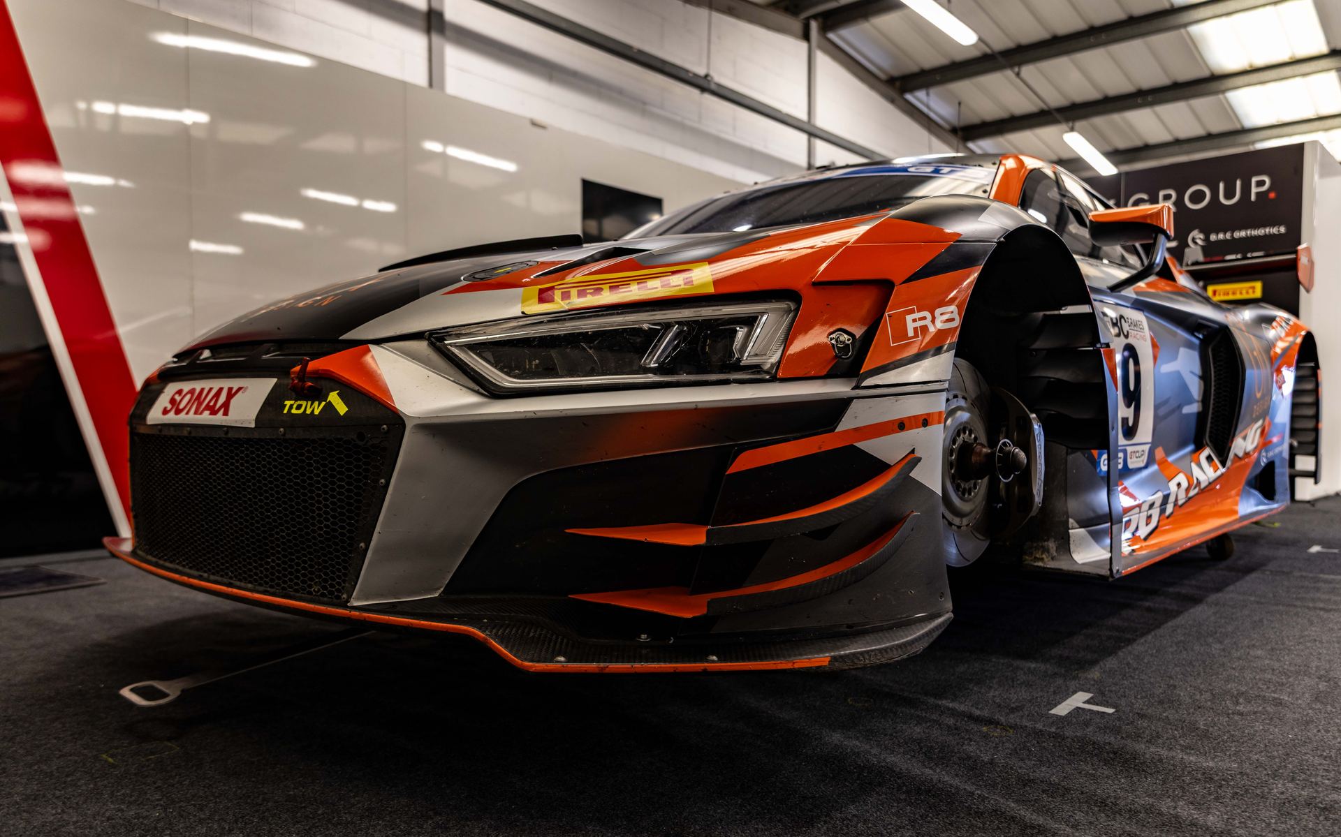 Close-up of the Audi R8 GT3's front end in the garage, sponsor board behind